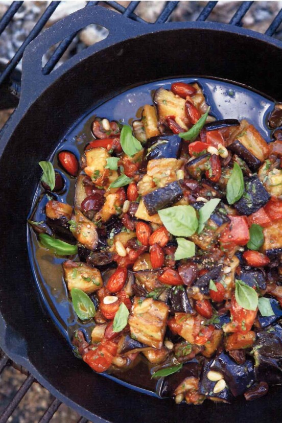 Skillet on a grill filled with eggplant caponata--chopped eggplant, onions, fennel, onions, almonds, basil