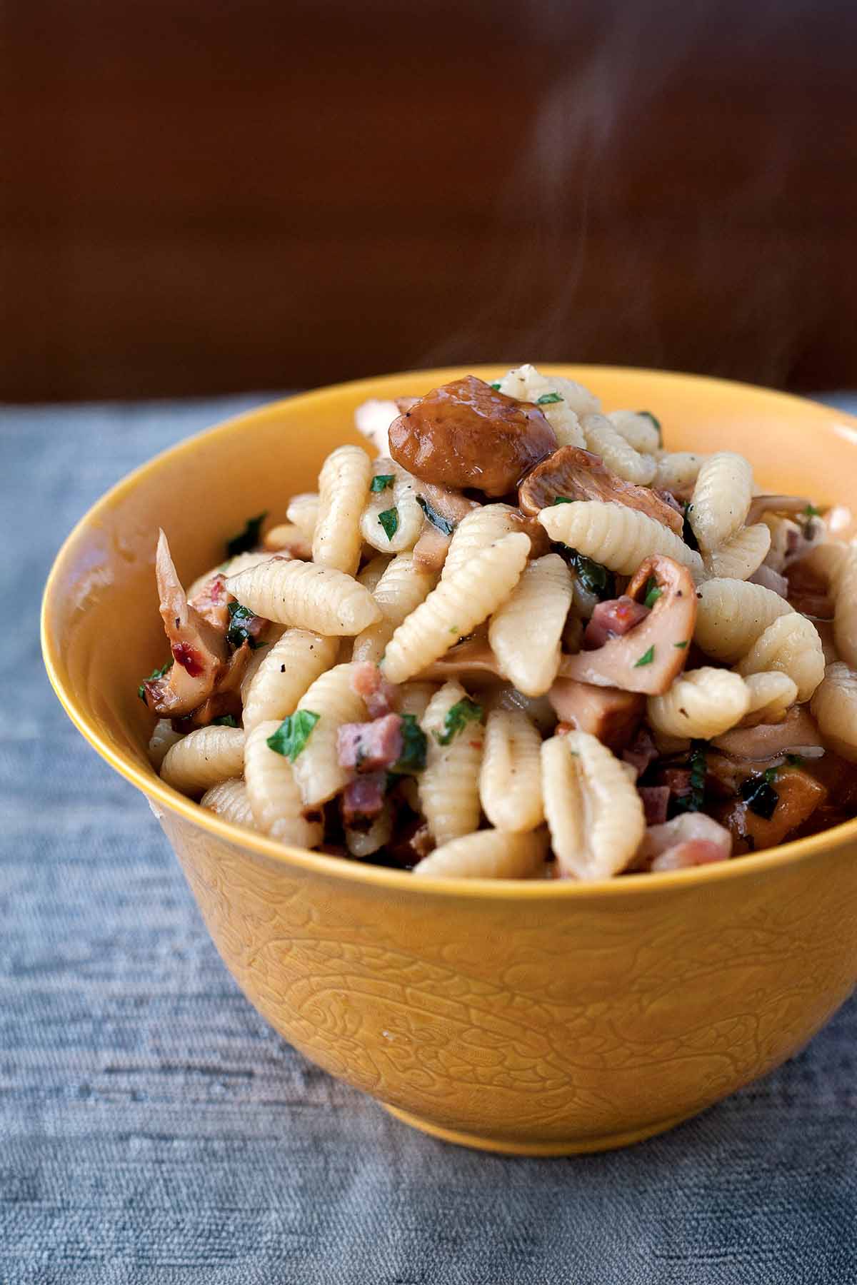 A yellow bowl of gnocchi-shaped pasta, with cured ham, mushrooms, and herbs.