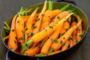 Oval pan with cumin-scented carrots sprinkled with chopped chives, orange zest, and pepper