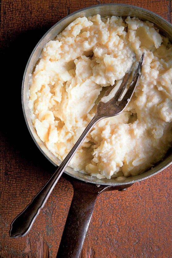 A pot of fork-mashed potatoes with a fork resting inside.