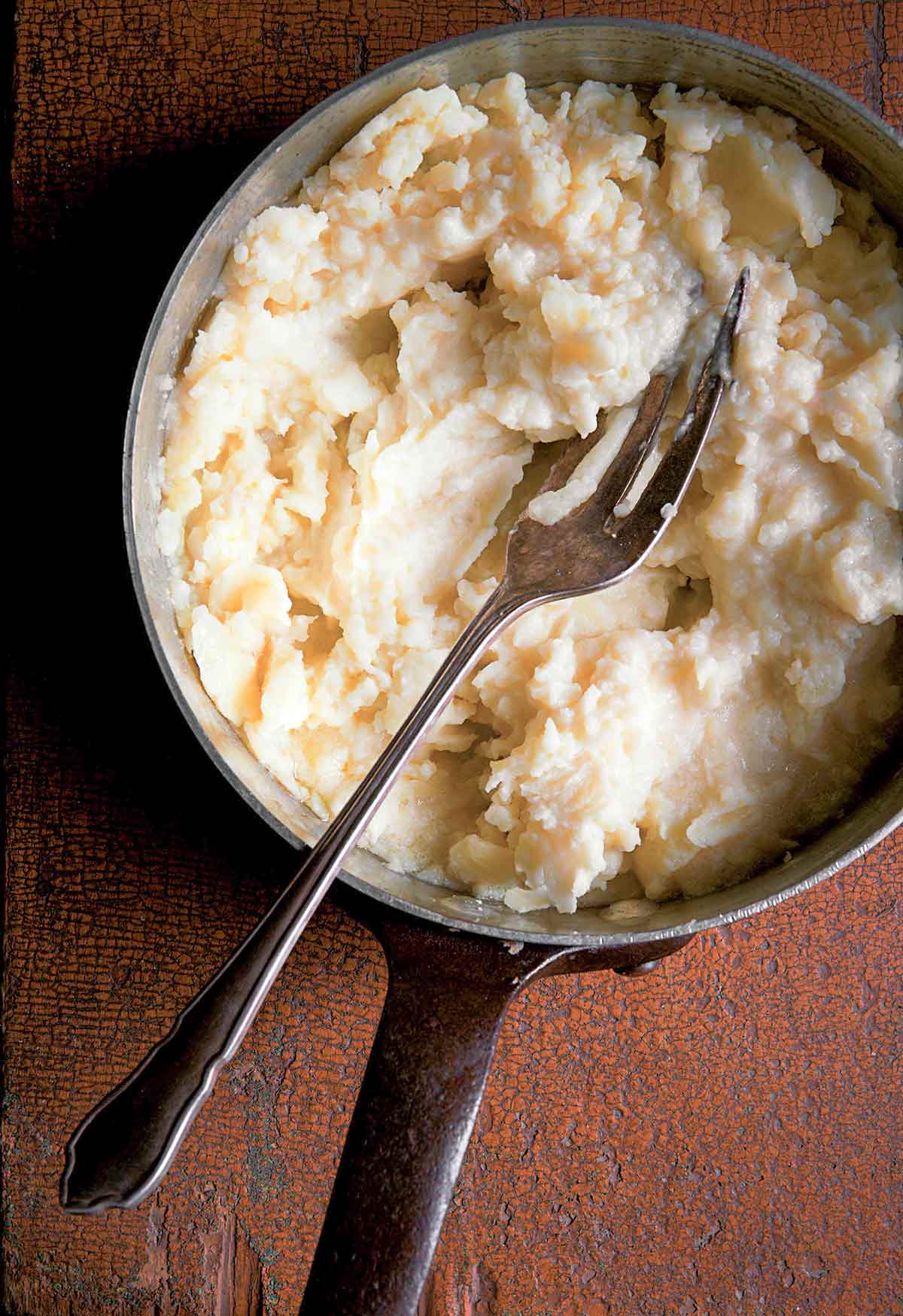 A pot of fork-mashed potatoes with a fork resting inside.