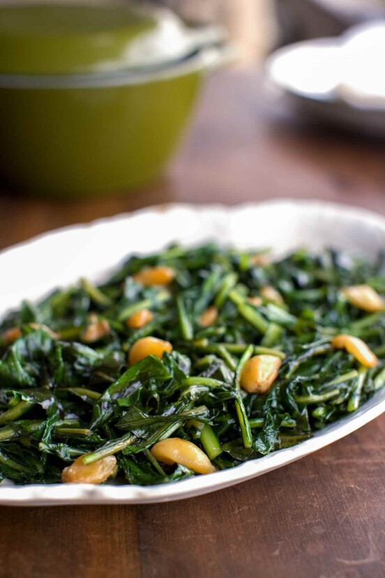 A white oval dish filled with dandelion greens sautéed in duck fat on a wooden table.