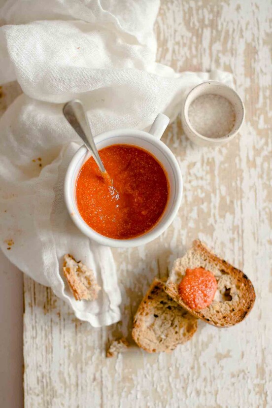 A white bowl of romesco sauce, a slice of bread nearby with the sauce on top.