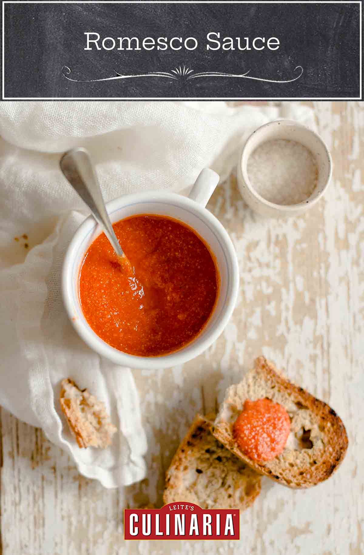 A white bowl of romesco sauce, a slice of bread nearby with the sauce on top.