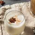 A glass filled with white bourbon milk with cinnamon sprinkled on top and with a star anise floating in the glass.