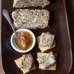 Chicken liver pate on a wooden tray with slices on toast beside a bowl of chutney.