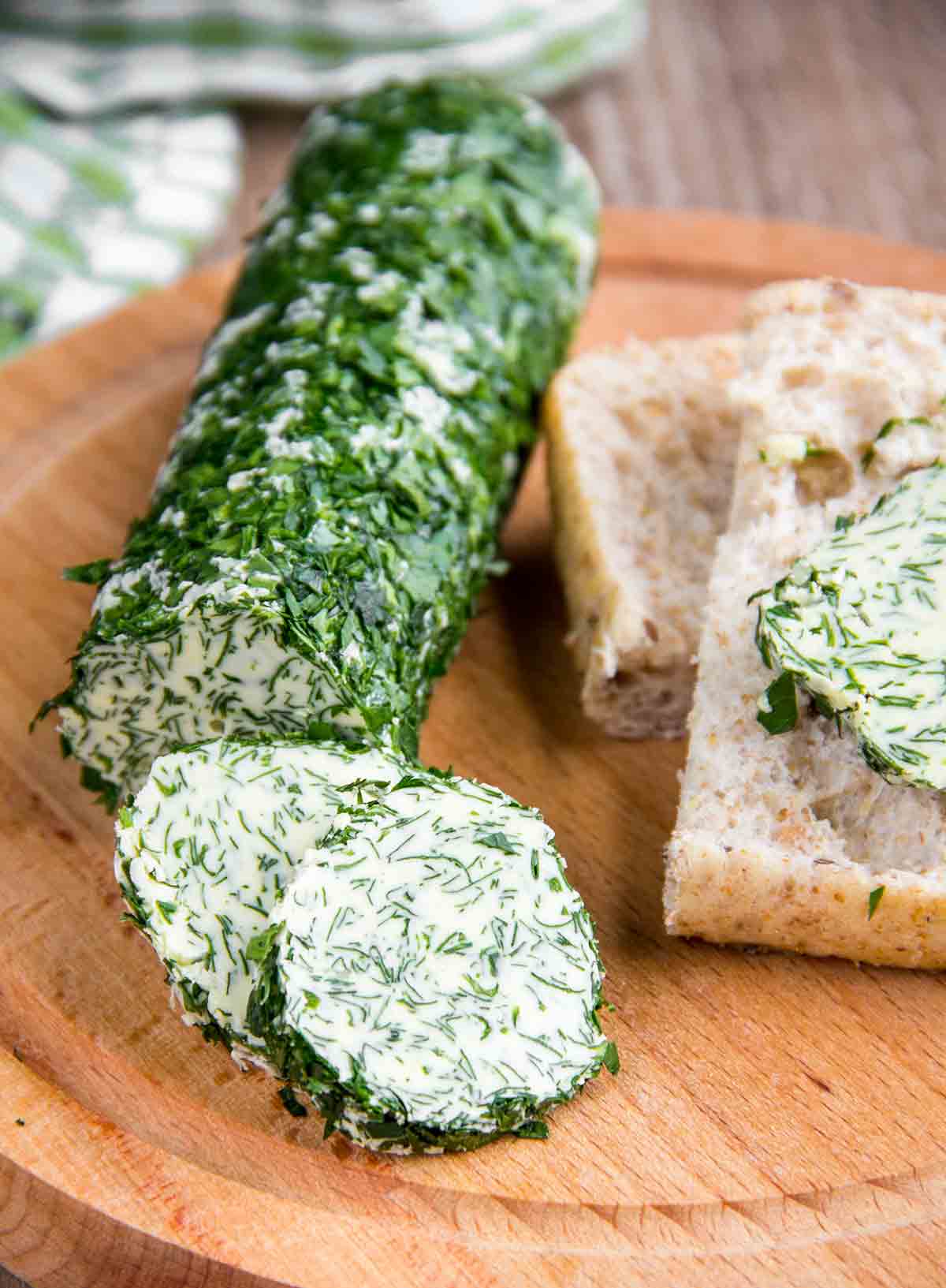 A log of maître d'hotel butter, covered in chopped parsley, on a cutting board, with bread on the side.
