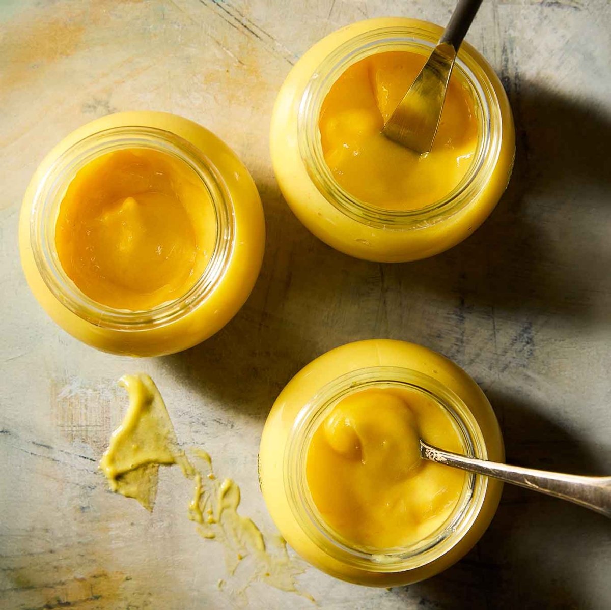 Three jars of homemade Meyer lemon curd, two with spoons in them.