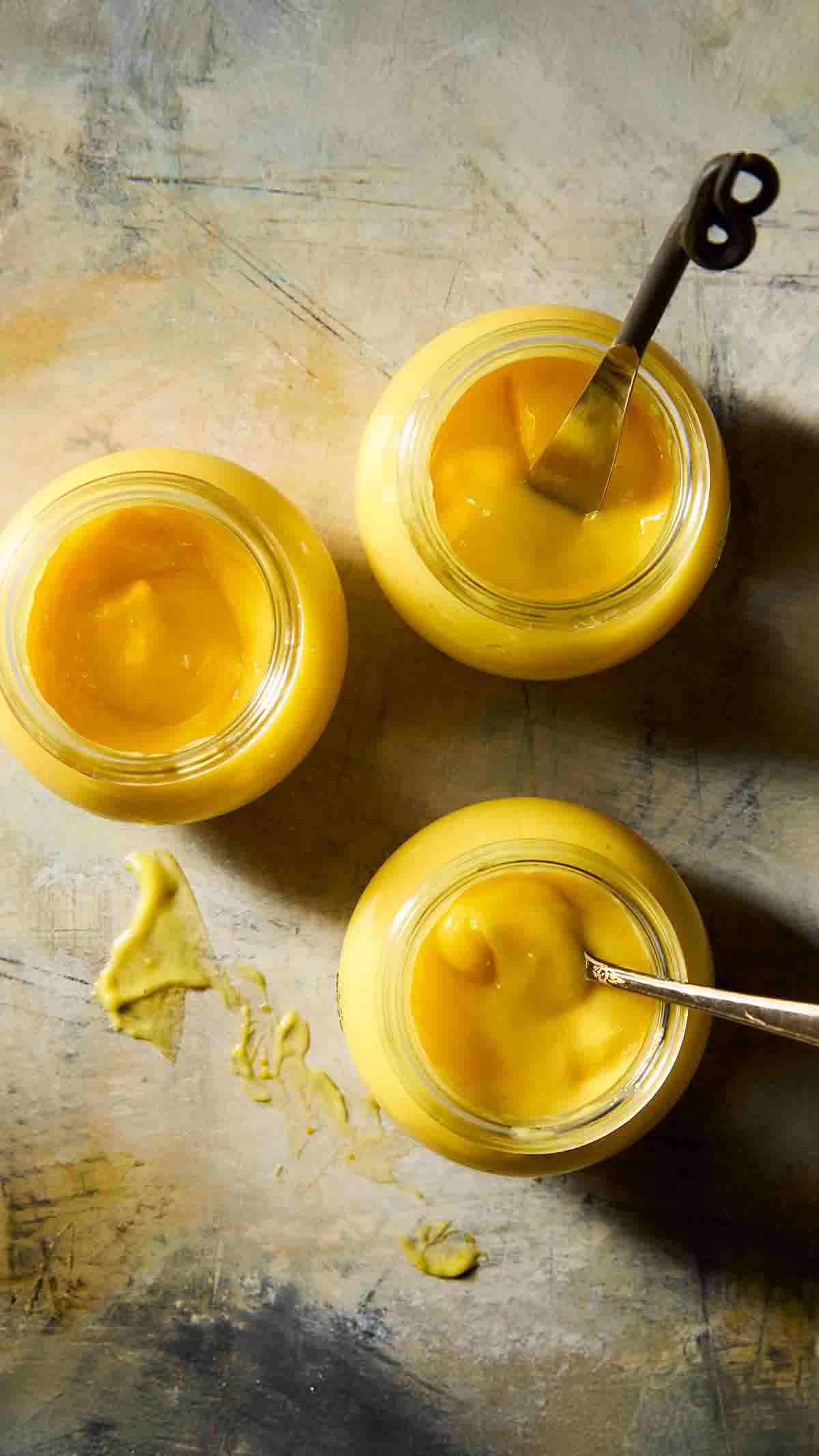 Three jars of homemade Meyer lemon curd, two with spoons in them.