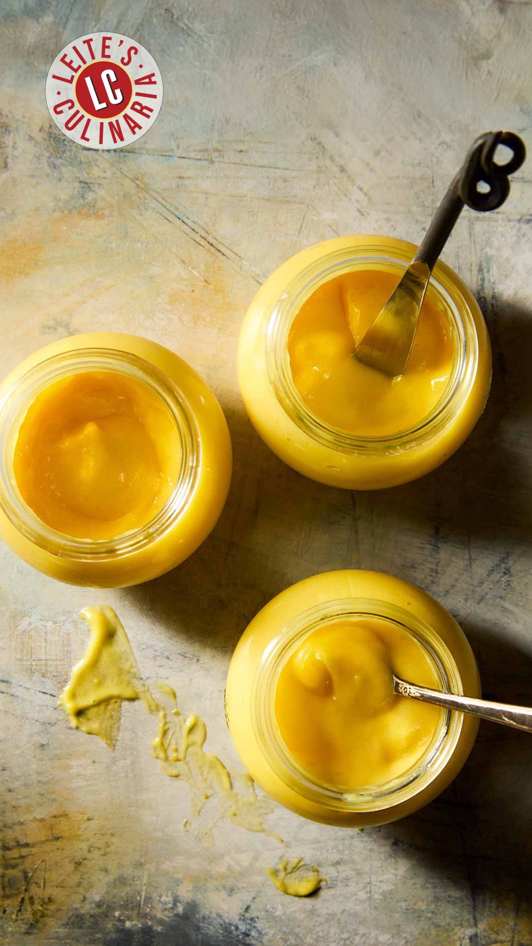 Three jars of homemade Meyer lemon curd, two with spoons in them.