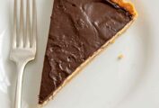 A slice of chocolate peanut butter tart with a cookie crust, peanut butter mousse filing, and a chocolate ganache topping