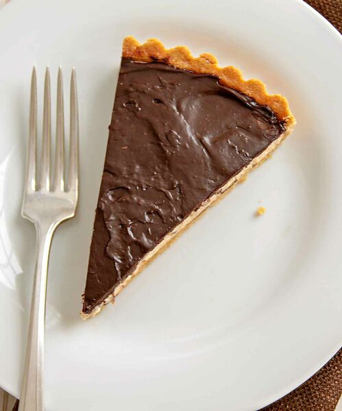 A slice of chocolate peanut butter tart with a cookie crust, peanut butter mousse filing, and a chocolate ganache topping