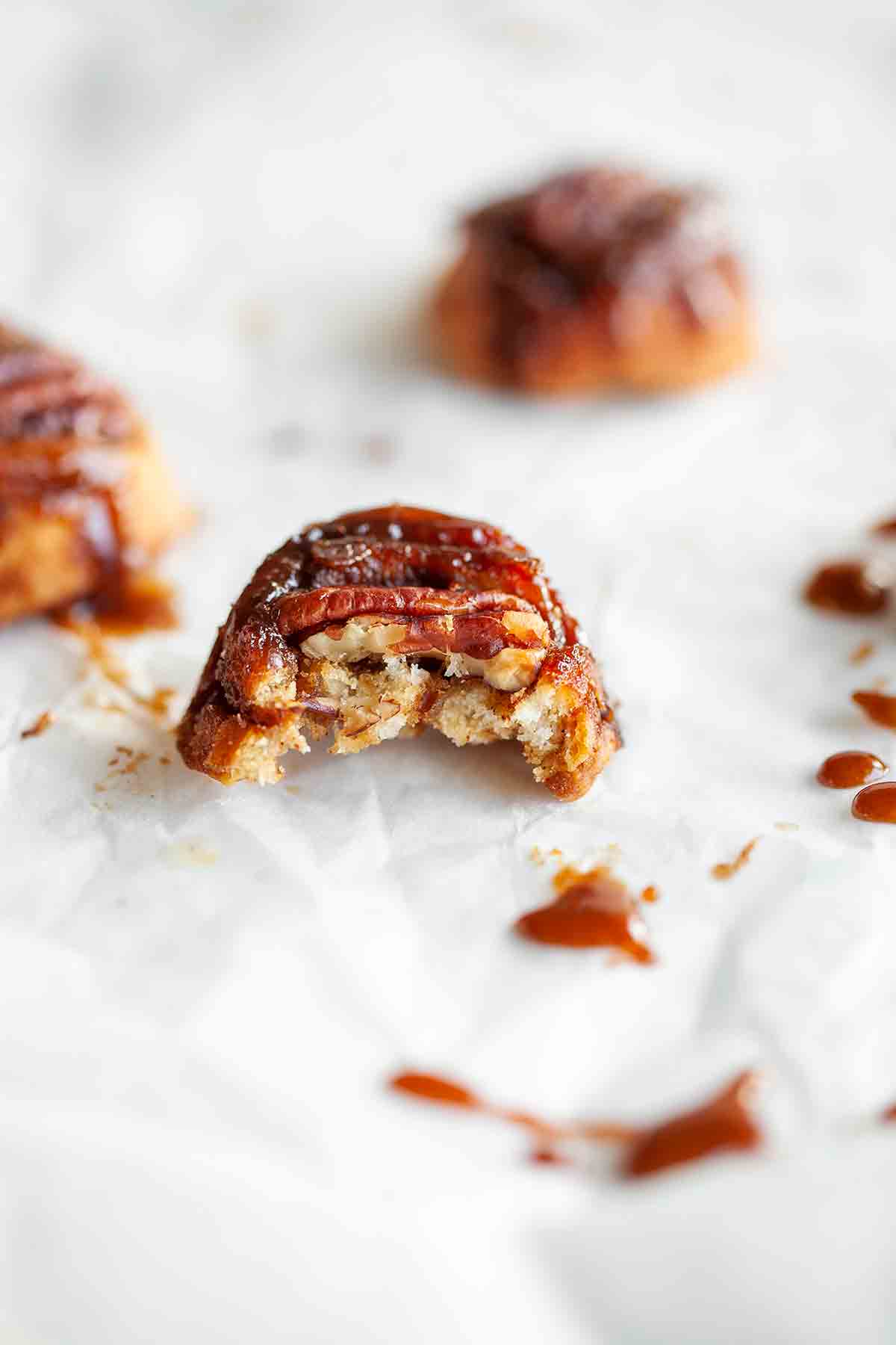 A half-eaten sticky pecan bite with a few in the background.
