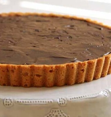Sweet peanut butter cookie tart crust filled with chocolate ganache, on a white plate