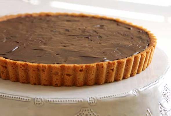 Sweet peanut butter cookie tart crust filled with chocolate ganache, on a white plate