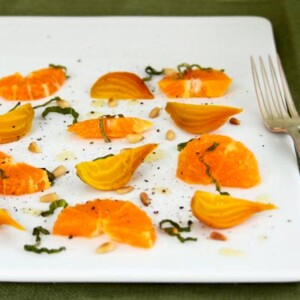 A rectangular white platter topped with tangerine and beet salad with basil garnish and a silver fork on the side.