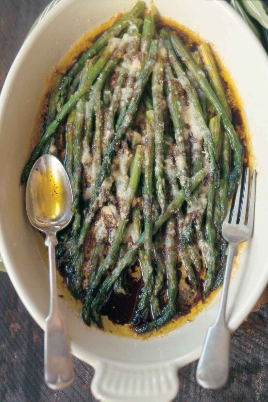 An oval serving dish filled with baked asparagus with Parmesan and balsamic vinegar with a fork and spoon resting on top.
