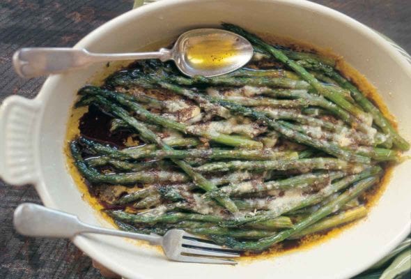 An oval serving dish filled with baked asparagus with Parmesan and balsamic vinegar with a fork and spoon resting on top.