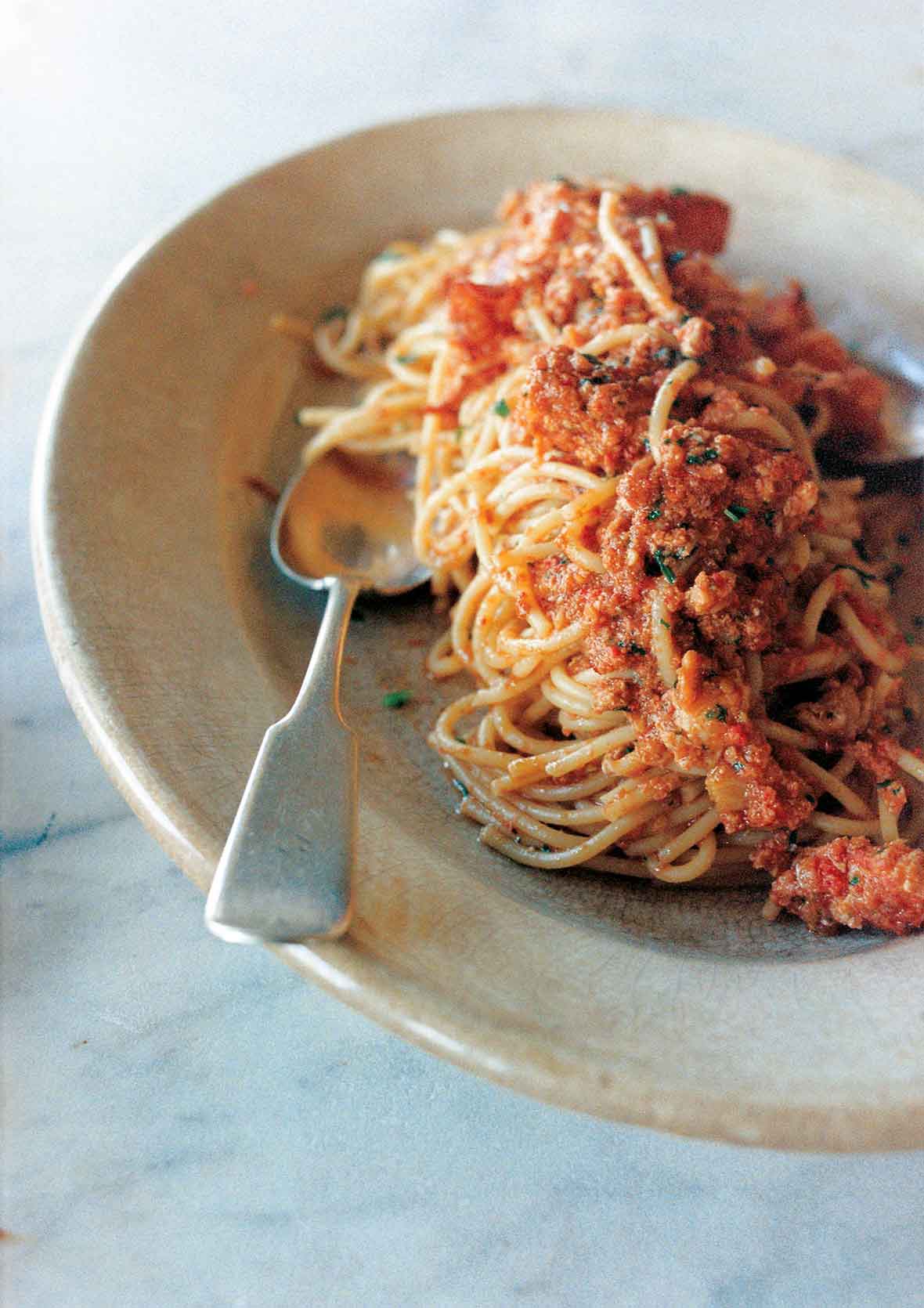 A serving of lobster fra diavolo in an oval bowl with a spoon resting inside.