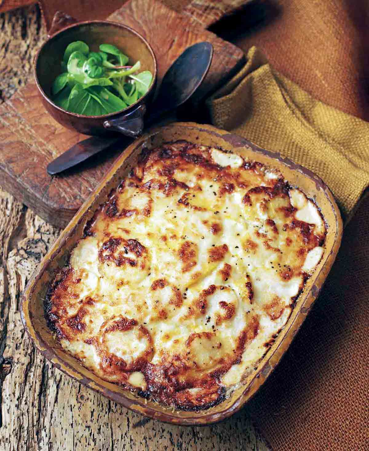 Casserole dish of root vegetable gratin topped with bubbly brown cheese on wood table