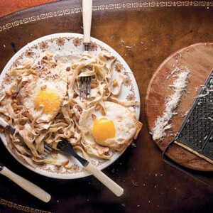 A tangle of brown butter pasta, toasted pine nuts, and two fried eggs on a plate with three forks in it.