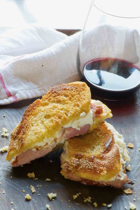 A three-cheese grilled cheese sandwich with ham that is cut in half with a glass of wine in the background.