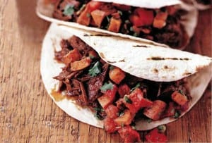 Two chipotle maple barbecue beef brisket tacos on a wooden surface.