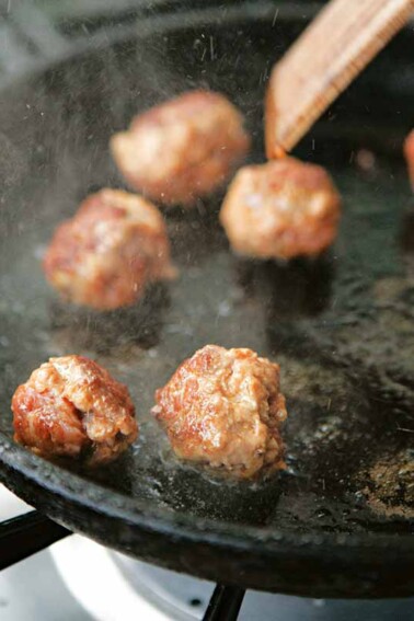 A cast-iron skillet with eight cheater's chorizo meatballs being cooked in it.