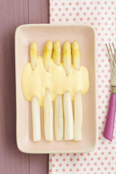 A plate of white asparagus with a quick blender hollandaise sauce on a polka-dotted fabric.