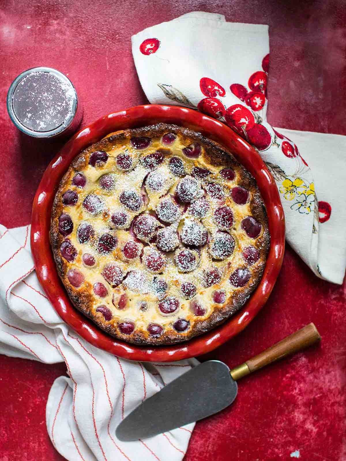 A cherry clafouti in a red dish with cherry dish towels