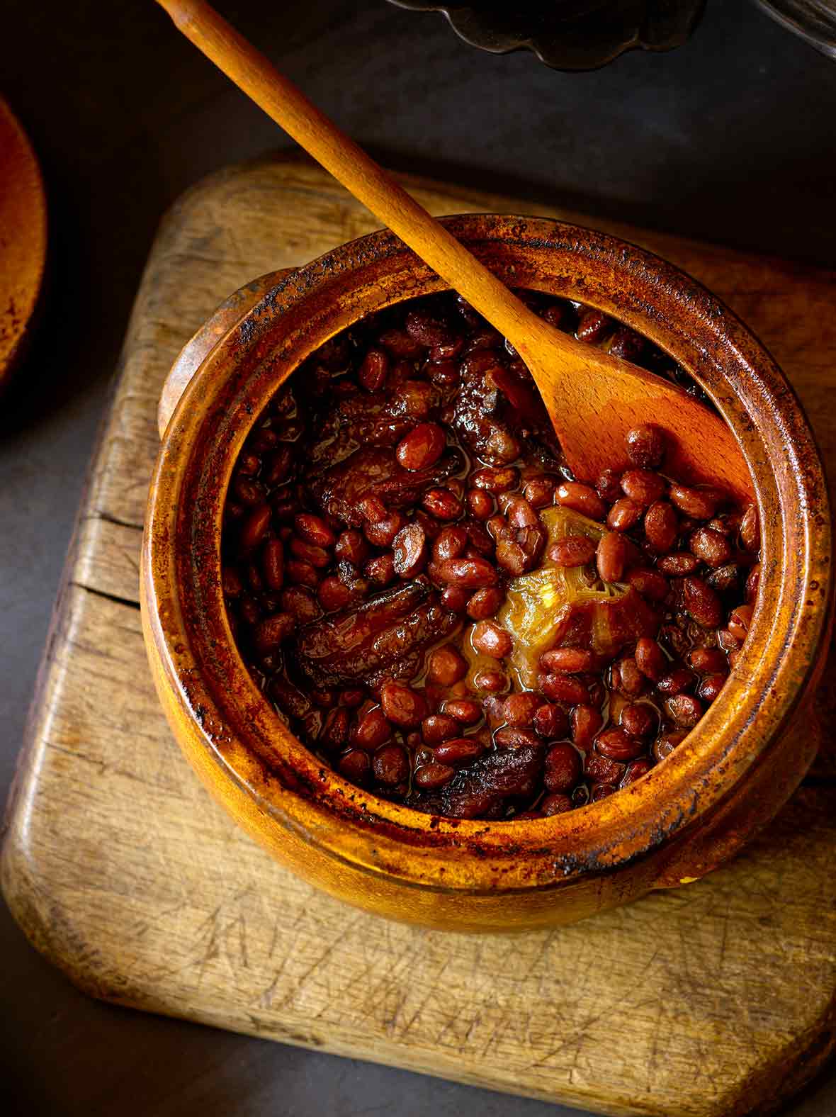 A bean pot of baked beans with a wooden spoon placed on a wooden chair