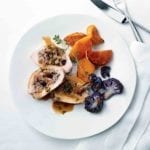 A sliced Mediterranean-style stuffed chicken breast on a white plate with purple cauliflower, sweet potato, and a sprig of thyme.