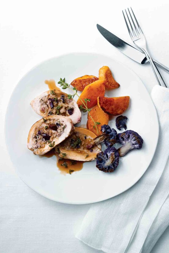 A sliced Mediterranean-style stuffed chicken breast on a white plate with purple cauliflower, sweet potato, and a sprig of thyme.