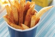A blue paper cup filled with beach fries that are sprinkled with Old Bay seasoning.