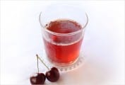 A glass filled with cherry spritzer and two cherries beside it.