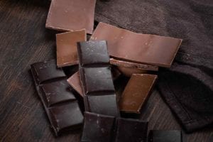 Pieces of dark and milk chocolate on a brown cloth and wood table in answer to the question of which chocolate: milk or dark?.