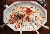An empty white plate with just smears of pasta sauce and a number of forks.