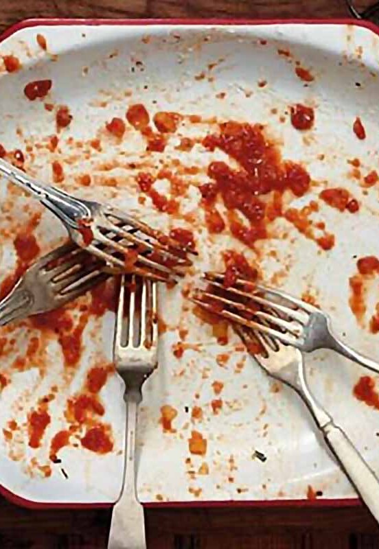 An empty white plate with just smears of pasta sauce and a number of forks.