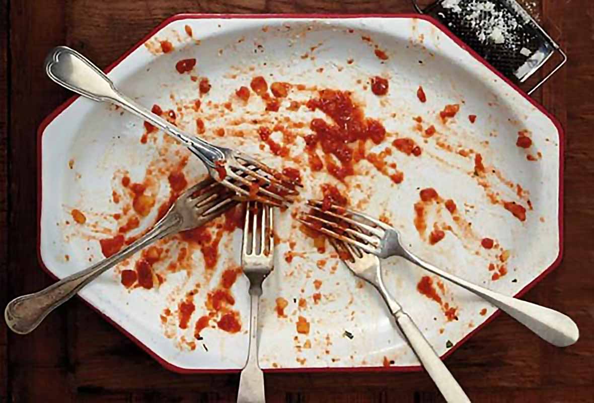 An empty white plate with just smears of pasta sauce and a number of forks.