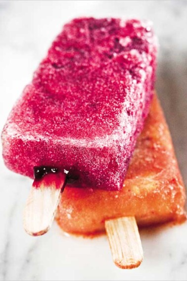 A hibiscus ice pop lying on top of a spicy mango ice pop.