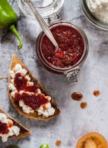 A Mason jar filled with apple-onion chutney along white crostini toped with goat cheese and more chutney