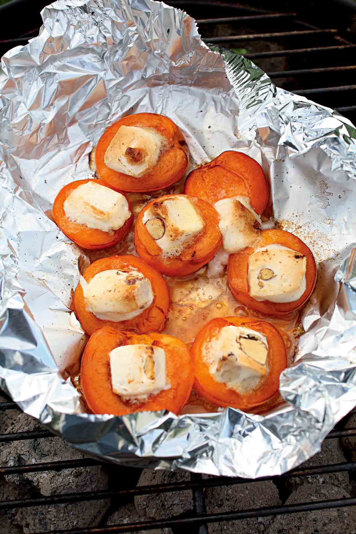 An open foil packet on the grill filled with grilled apricots with gooey nougat in the center.