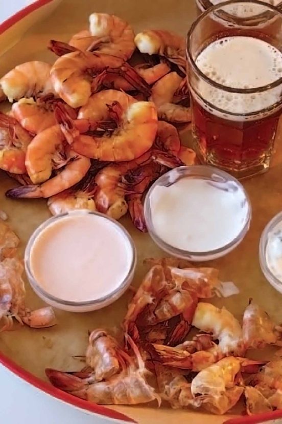 Shrimp with three dipping sauces piled on a platter, beside a glass of ale