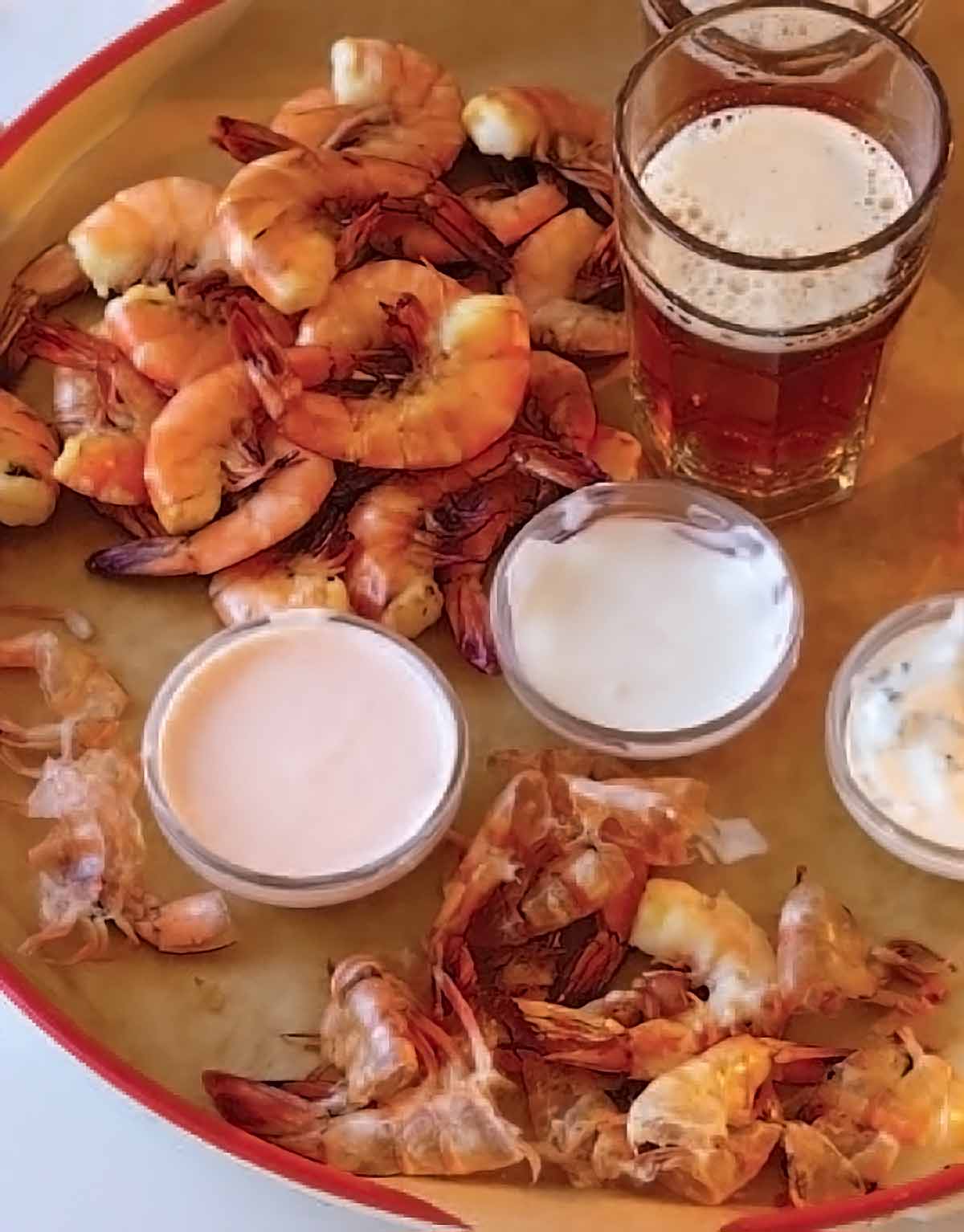 Shrimp with three dipping sauces piled on a platter, beside a glass of ale