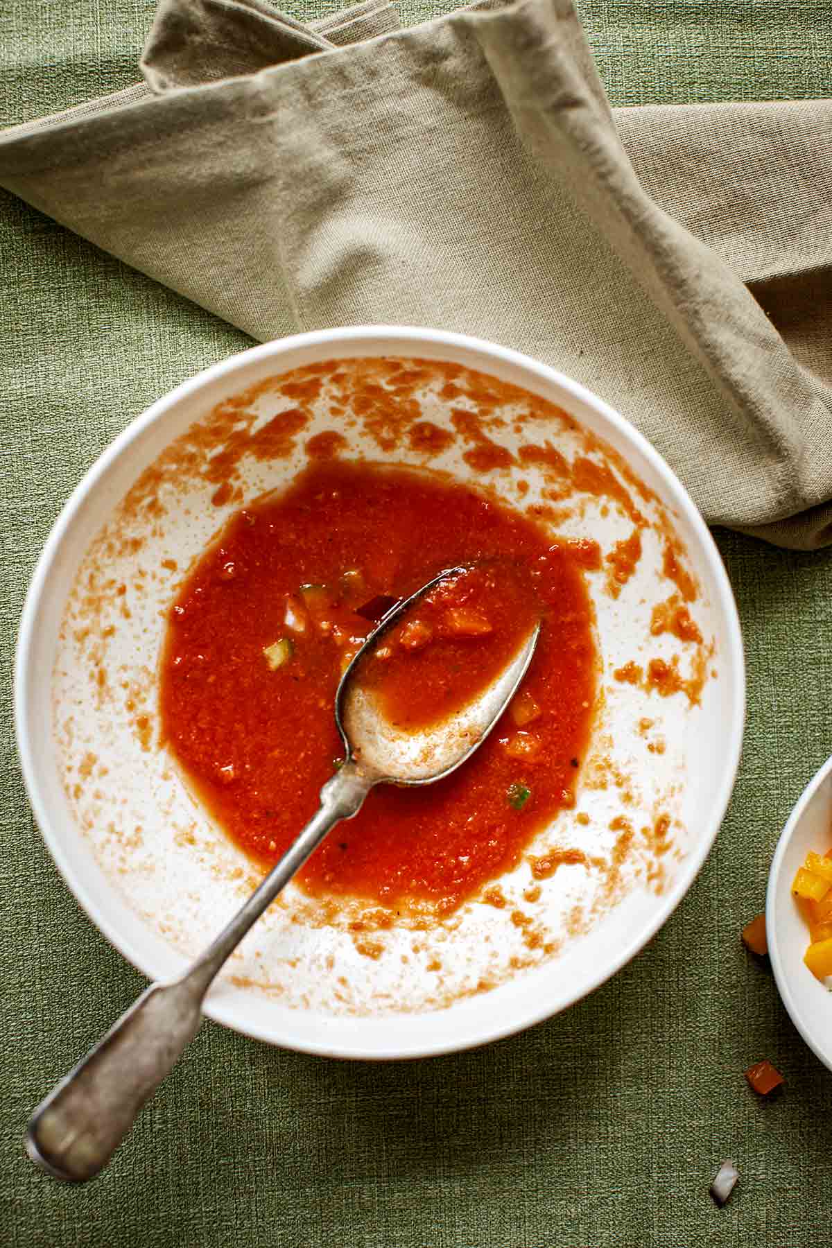An almost empty bowl of Spanish gazpacho with a spoon resting inside.