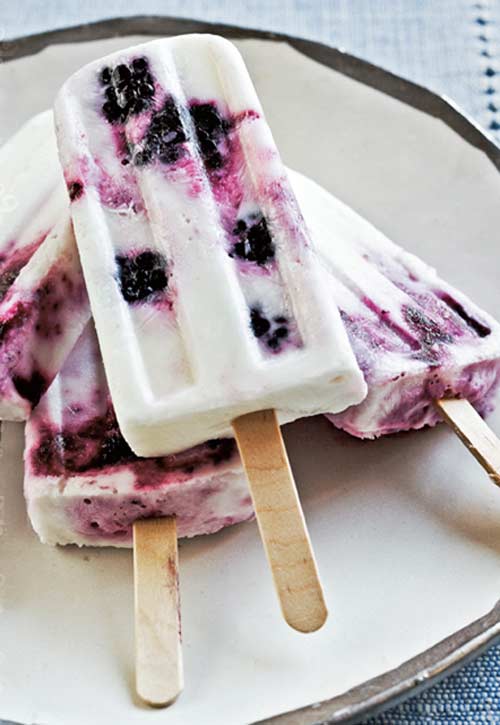 Yogurt ice pops with berries stacked on a white plate.