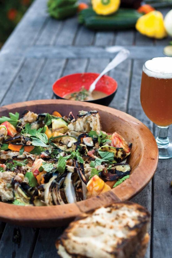 A wooden bowl filled with Catalan bread salad and a frothy beer on the side.