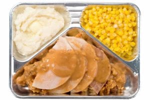 A tv dinner with sliced meat, stuffing, gravy, corn, and mashed potatoes in a foil container.