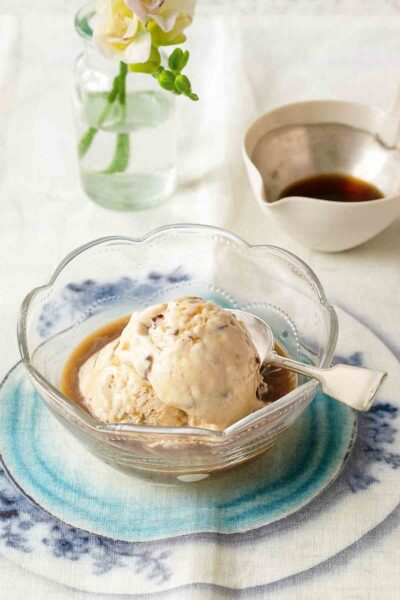 Butter pean affogato--butter pecan ice cream and espresso--in a glass bowl with a spoon, on a floral tablecloth.