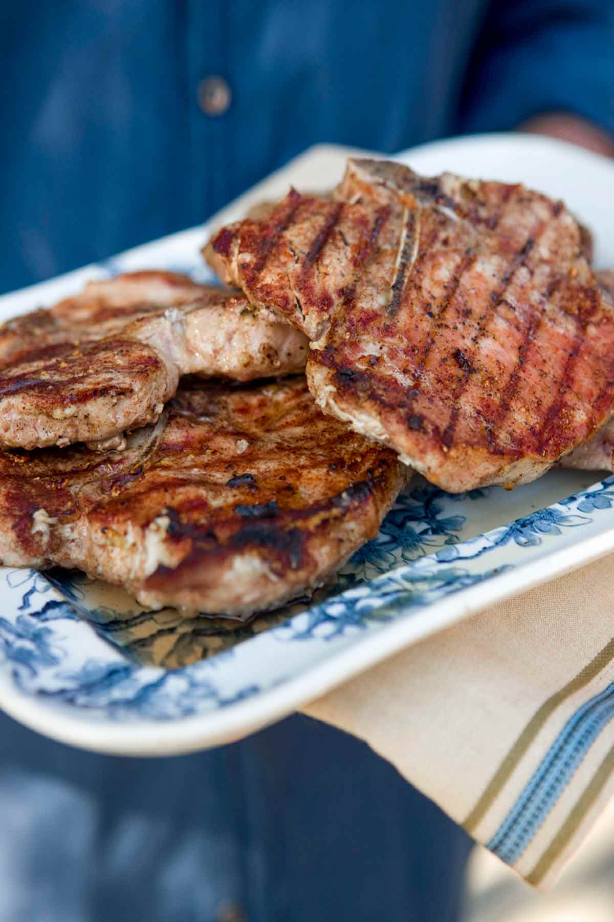 A person carrying a decorative blue and white serving platter loaded with five-spice grilled pork chops.